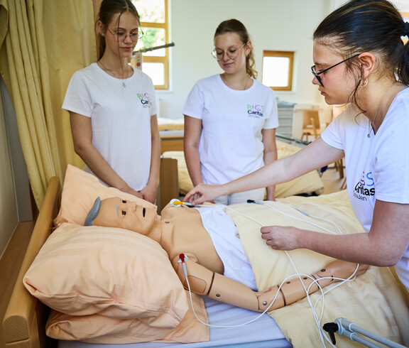 Schüler*innen im Pflegeunterricht legen einer Puppe ein EKG an