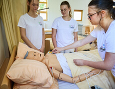 Schüler*innen im Pflegeunterricht legen einer Puppe ein EKG an
